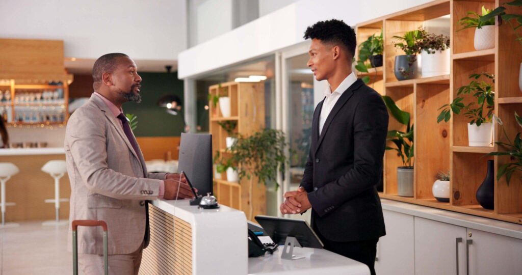 Hotel, lobby and man with receptionist for booking, guest room service and reservation. Hospitality, front desk and person talking with concierge for check in, accommodation and sign in with suitcase